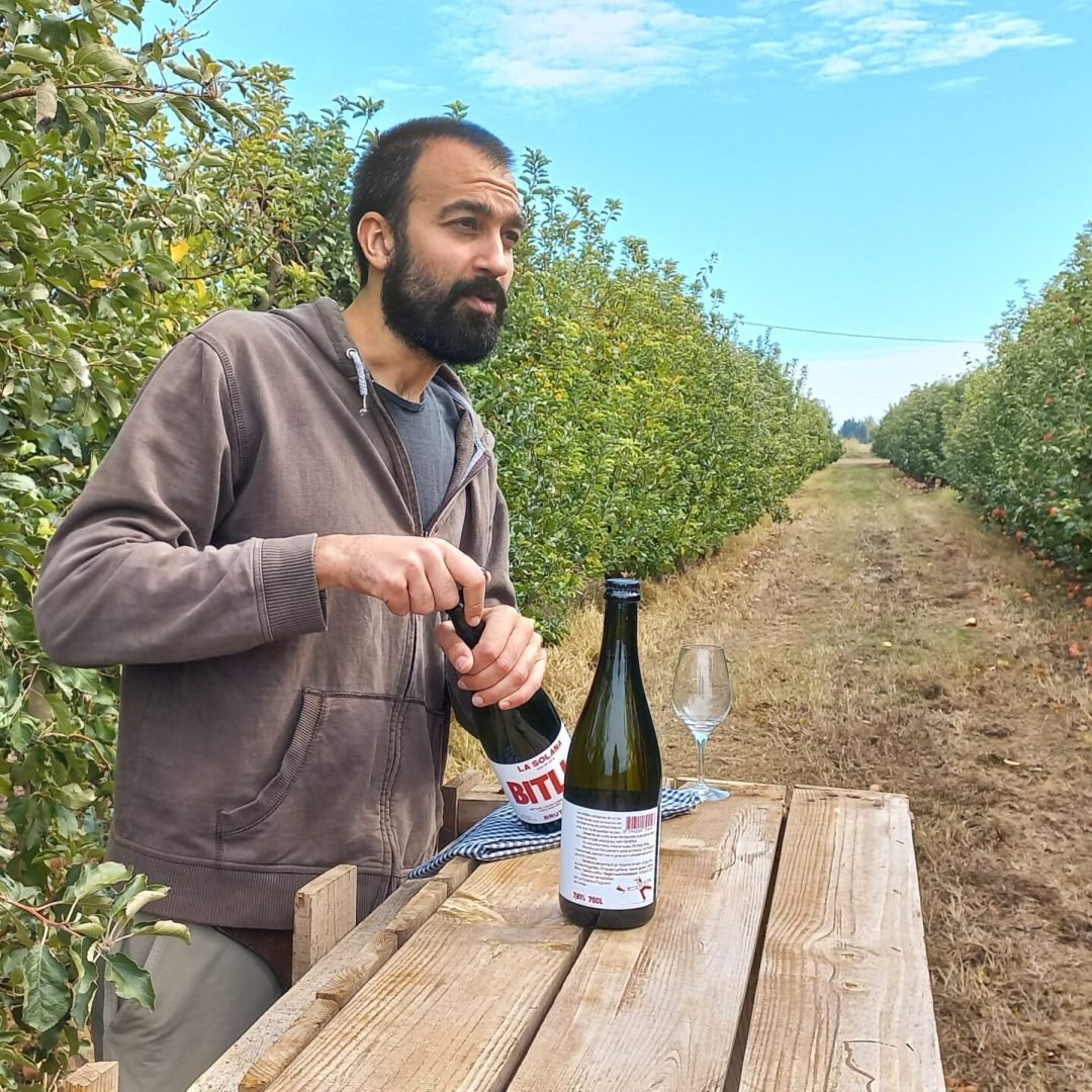 hombre abriendo una botella de biela sidra la solana en medio de unas viñas